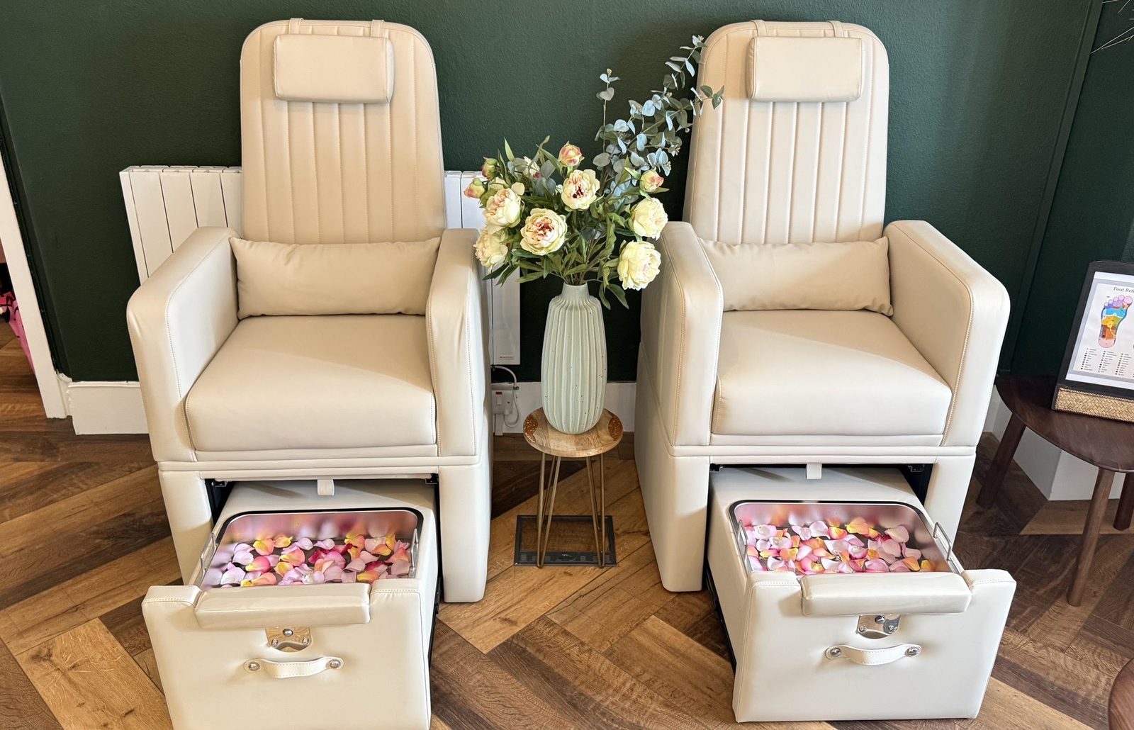 Two cream foot massage chairs with rose petal footbaths, against a deep green wall