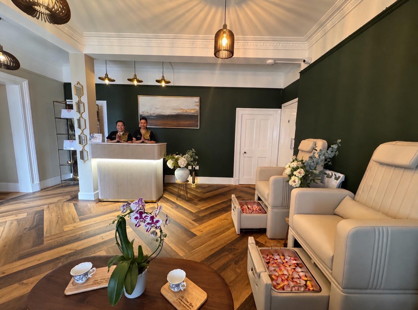 Two therapists welcoming guests at the Isle View Spa reception desk, with foot massage chairs alongside